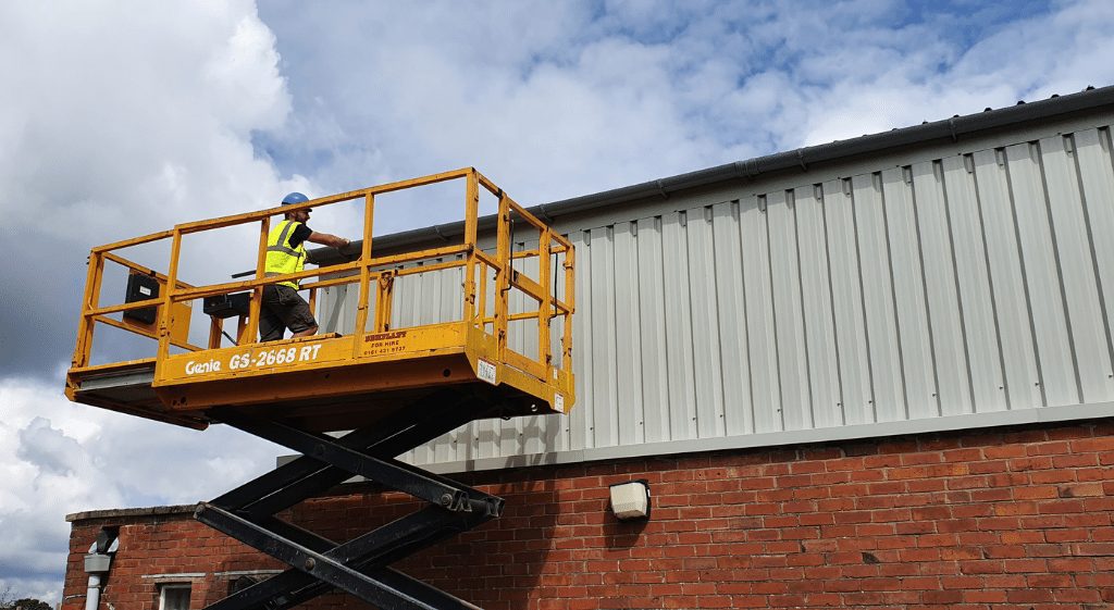 A construction worker on a powered access platform inspecting sheet cladding during his Cladding NVQ