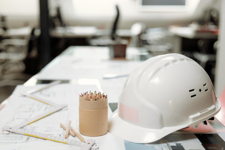 Construction hard hat on top of building plans and NVQ qualification plans.