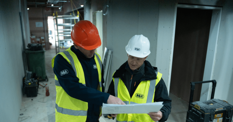 Man in an orange hat and man in a white hat looking at a board