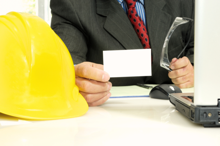 Construction manager holding out a CSCS card with a yellow hard hat helmet next to him.